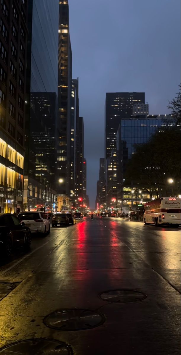 an empty city street at night with cars parked on the side and tall buildings in the background