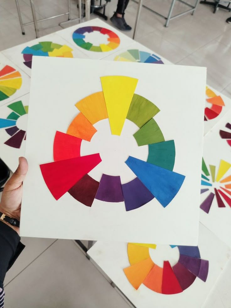 a person holding up a piece of paper that has been cut into color wheel shapes