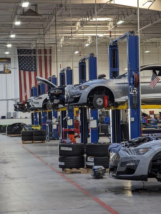 an assembly line with cars on lifts and american flag hanging from the ceiling in the background