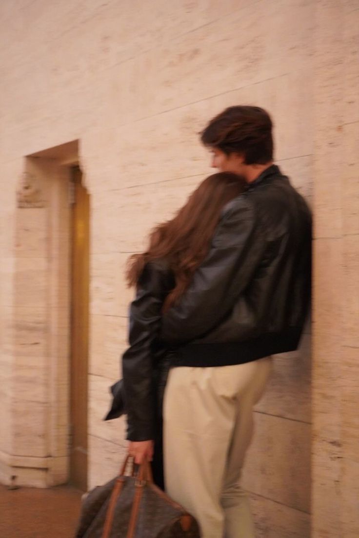 a woman standing next to a wall with a handbag on her hip and looking down at the ground