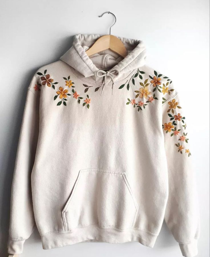 a white hoodie with flowers on it hanging from a hanger against a wall