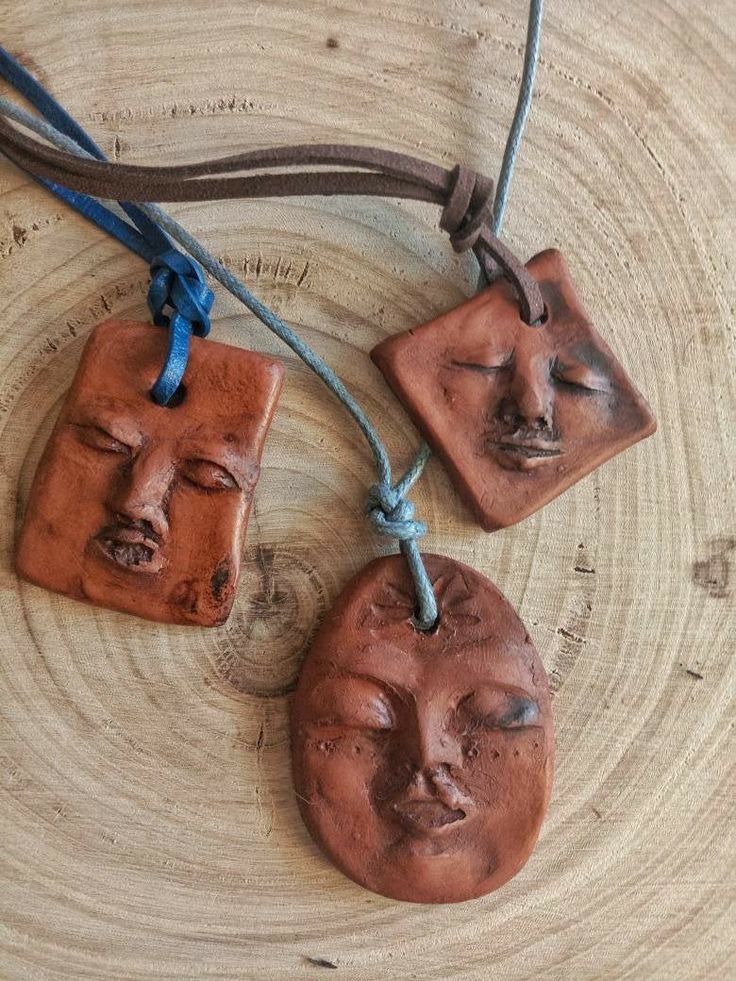 three clay faces hanging from strings on a piece of wood