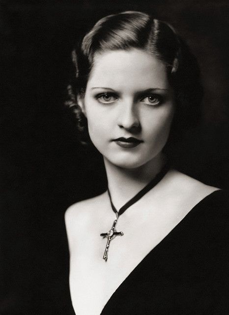 an old black and white photo of a woman wearing a cross necklace