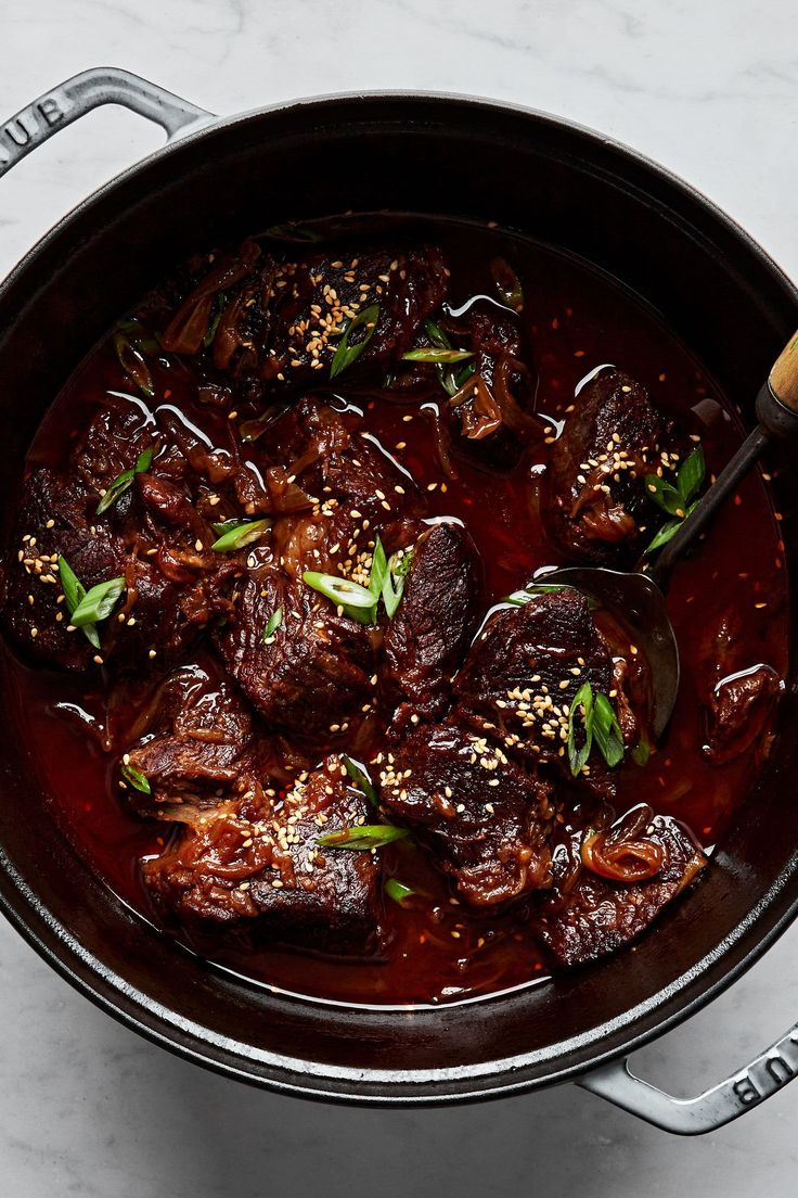 a pot filled with meat and sauce on top of a counter next to a wooden spoon