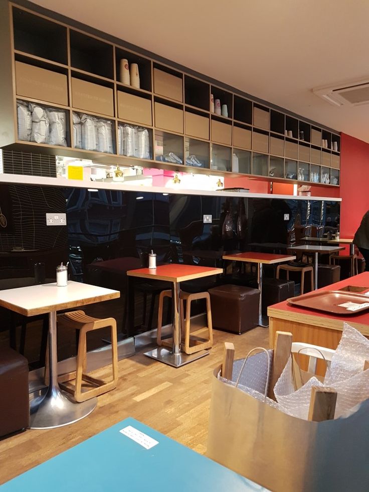 an empty restaurant with tables and stools in the foreground, shelves on the far wall