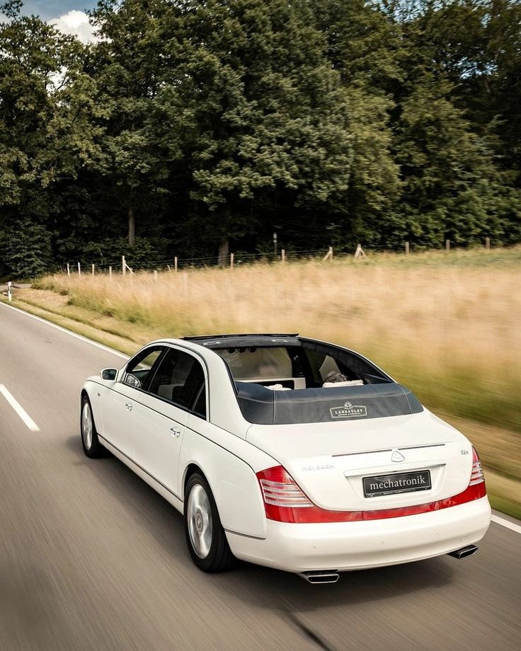 a white car driving down the road with trees in the backgrouund and grass on both sides