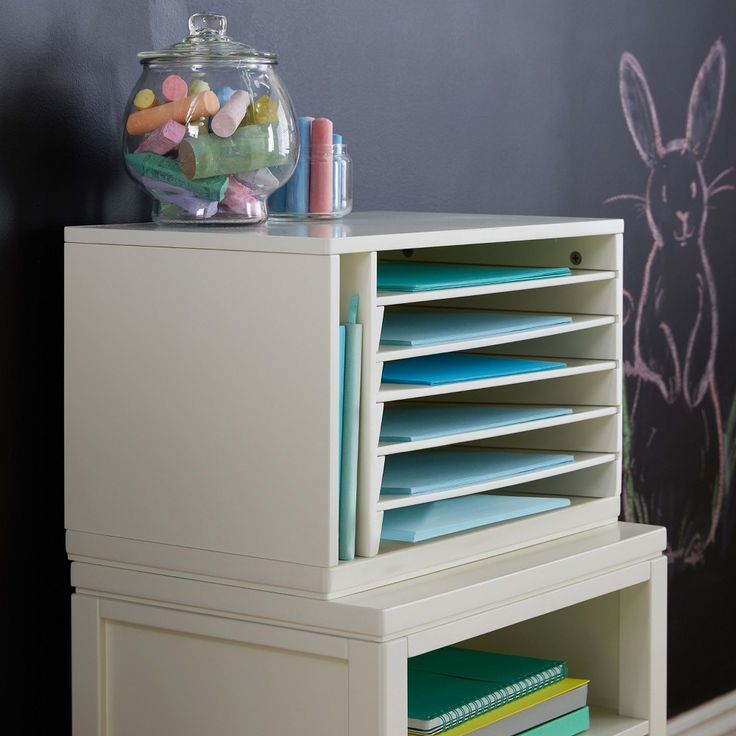 a white desk with lots of books on top of it next to a chalkboard wall