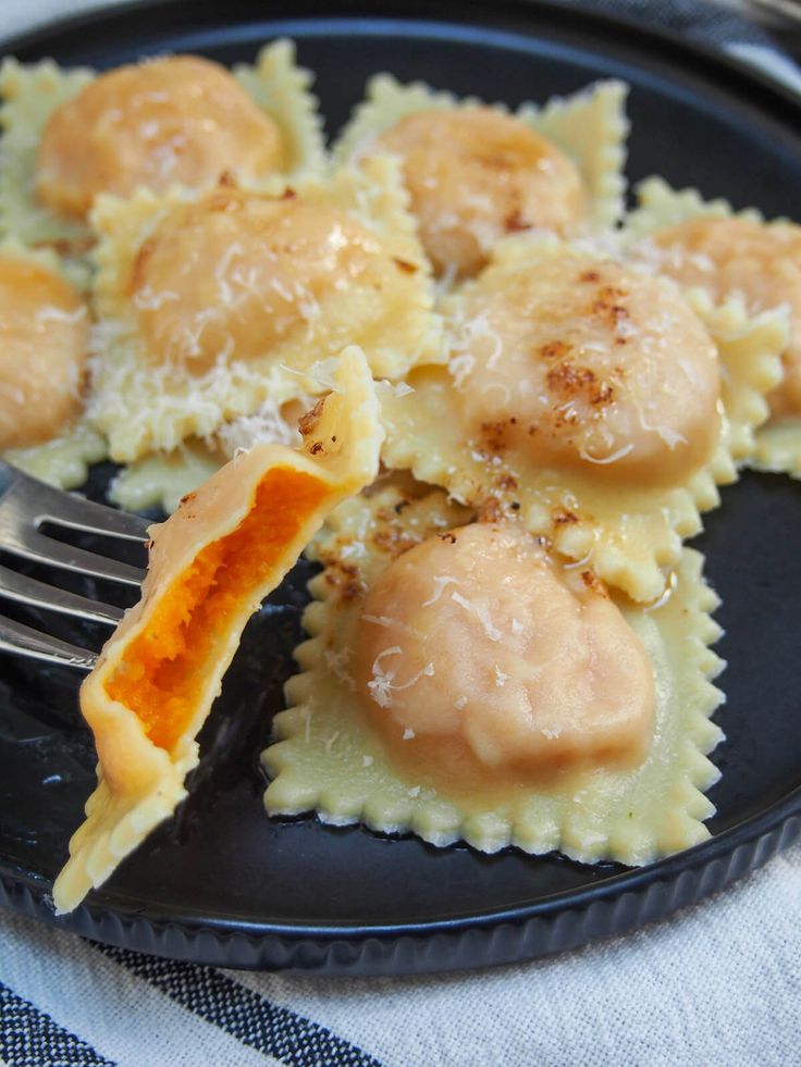 a black plate topped with ravioli covered in gravy next to a fork