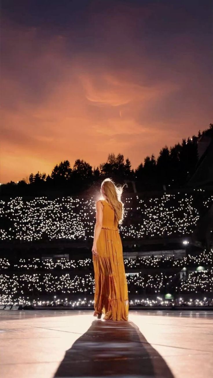 a woman in a yellow dress is standing on a platform at night with the sun setting behind her