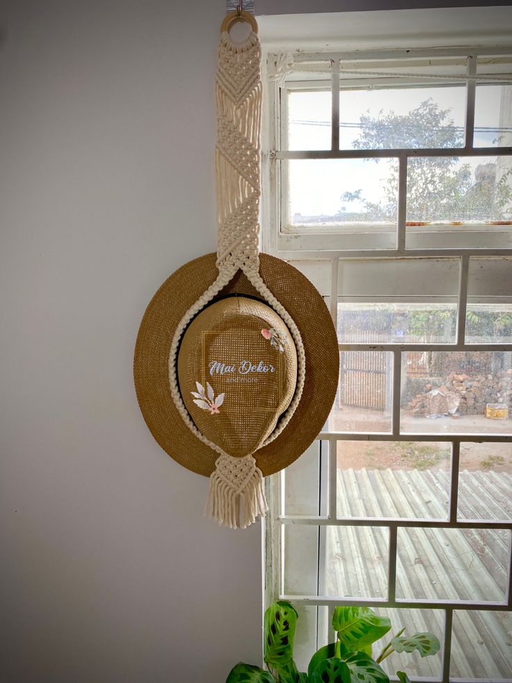 a hat hanging from the side of a window next to a green potted plant