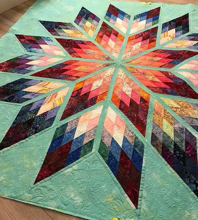 a quilted table topper on the floor in front of a wooden floor with a blue background