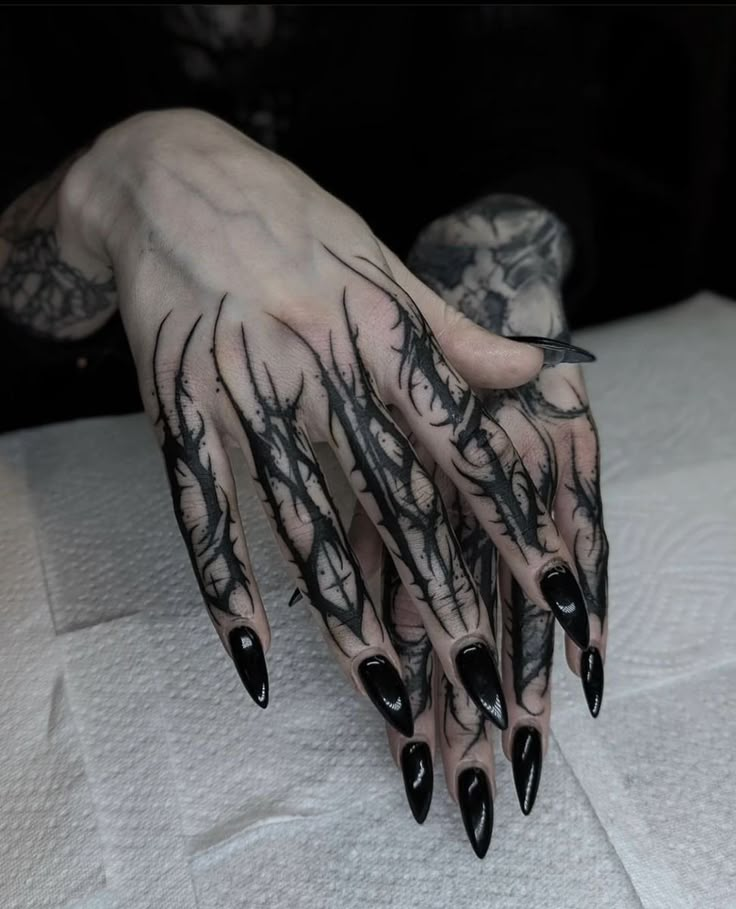 a woman's hand with black nail polish and tattoos on her left arm, sitting on a white sheet