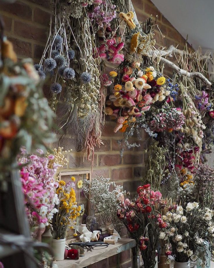 a room filled with lots of different types of flowers hanging from the ceiling next to a brick wall