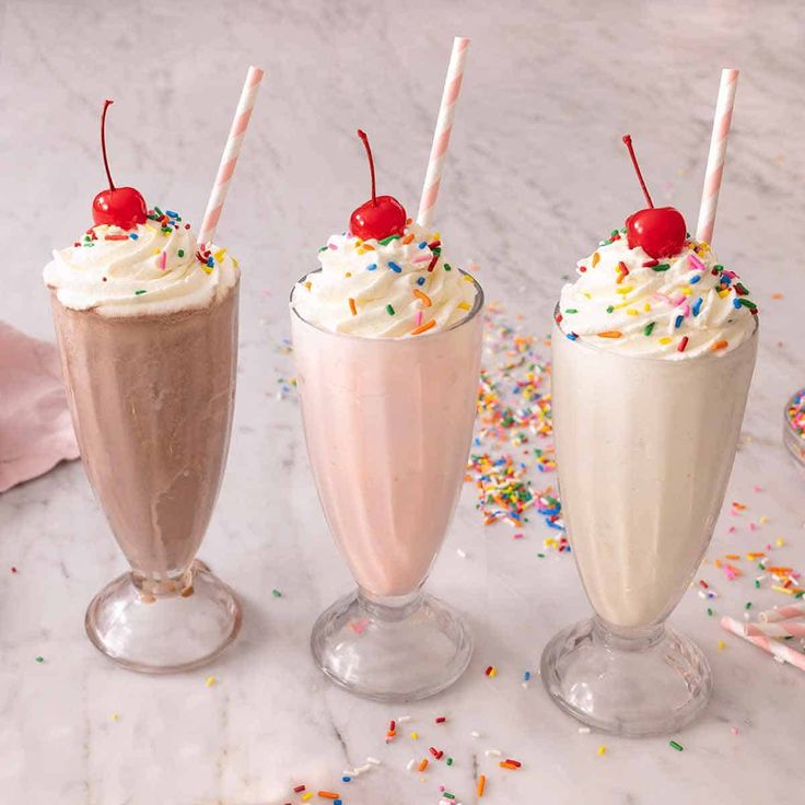 three milkshakes with sprinkles and cherries in them on a table