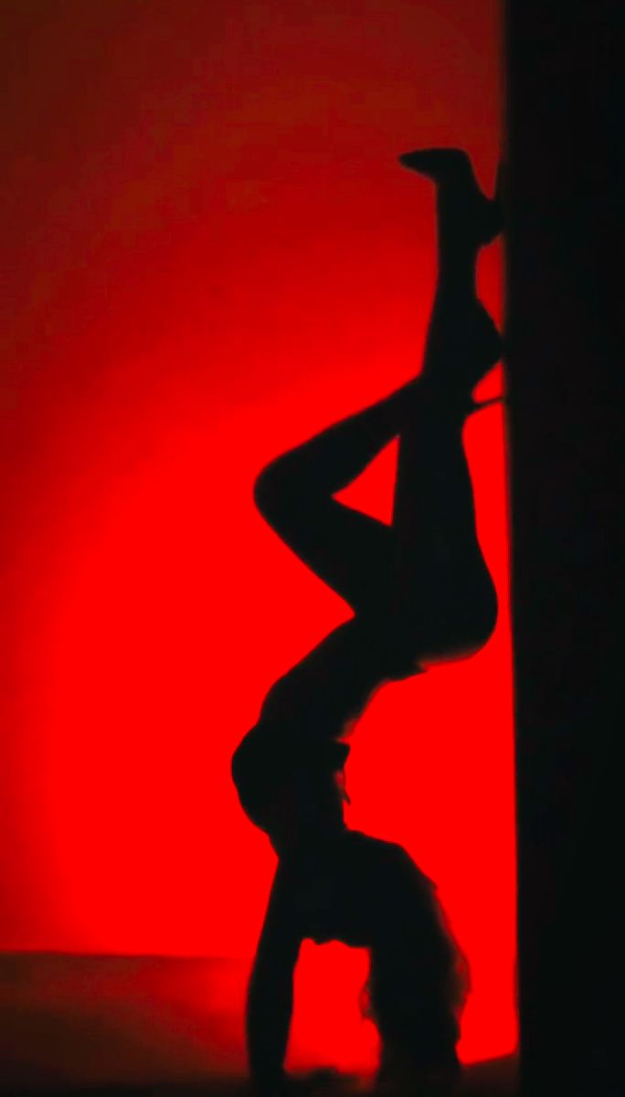 the silhouette of a woman leaning against a wall in front of a red background,