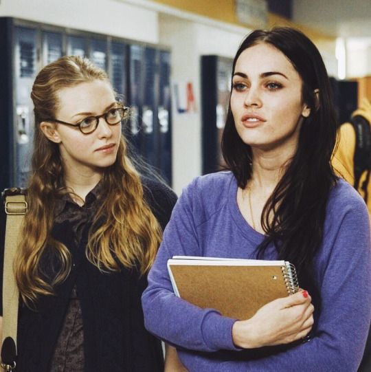 two young women standing next to each other in a hallway with lockers behind them