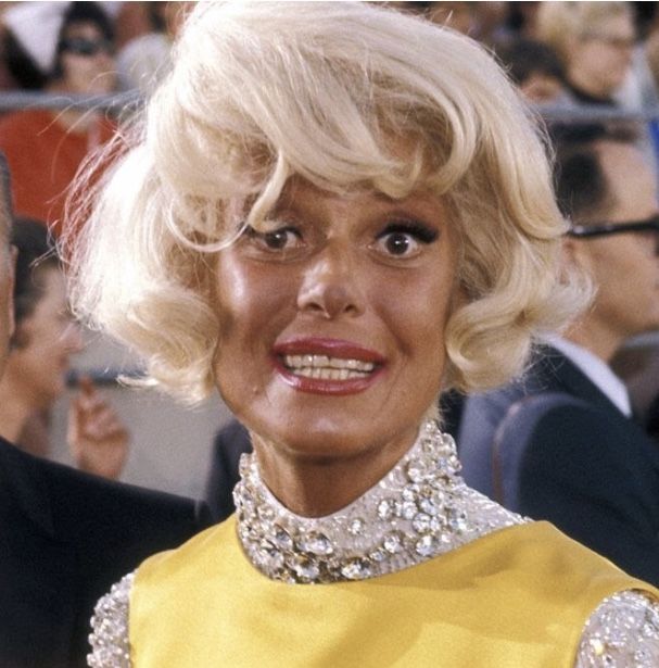 a woman with blonde hair wearing a yellow dress and diamond collared necktie in front of an audience