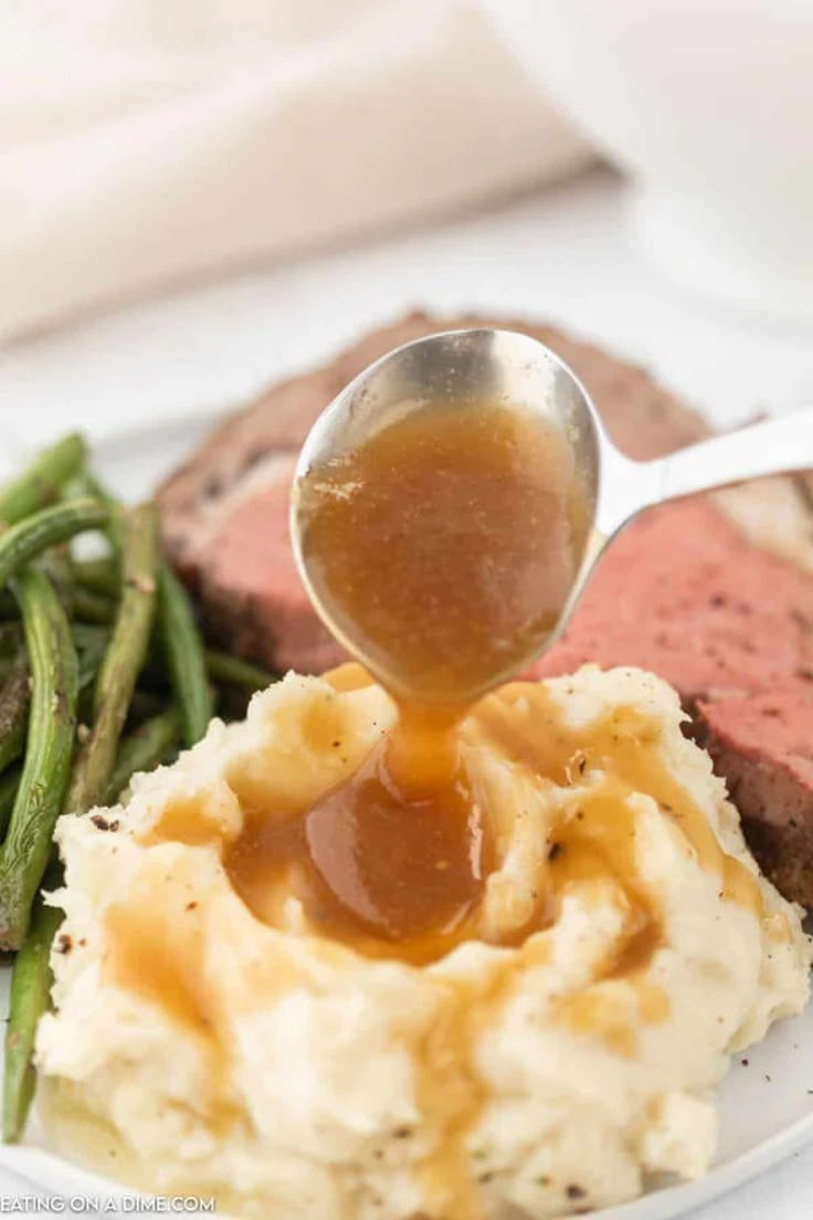 a spoon drizzling sauce over mashed potatoes and green beans on a plate