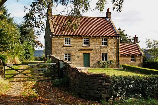 an old stone house with a gate in the foreground and green grass on the other side