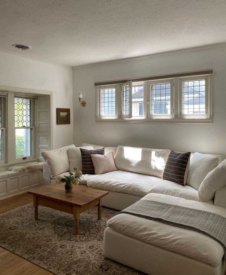 a living room with white couches and pillows on the floor in front of two windows