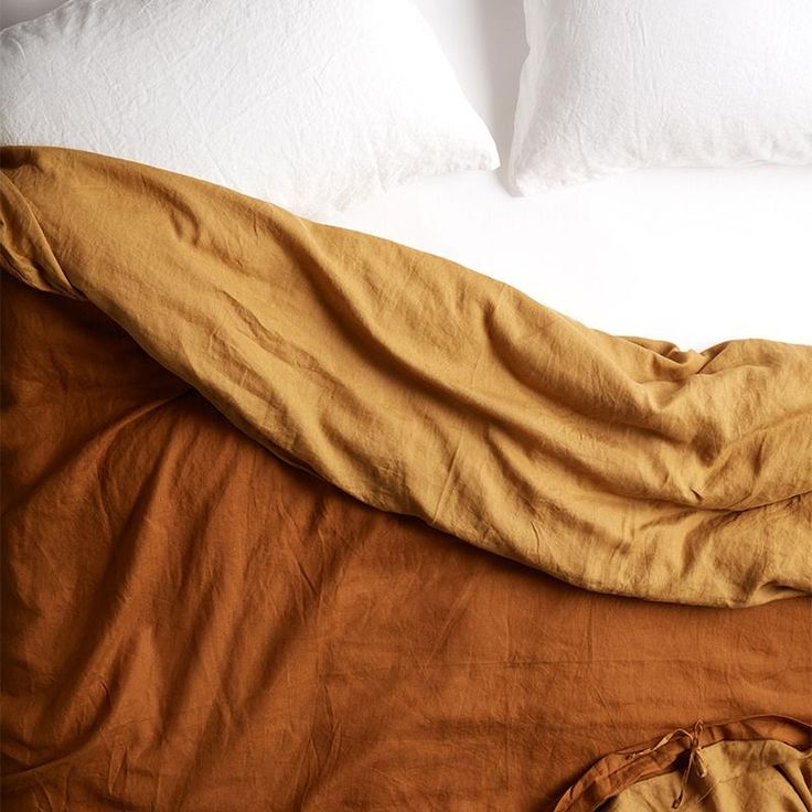 an unmade bed with brown sheets and white pillows