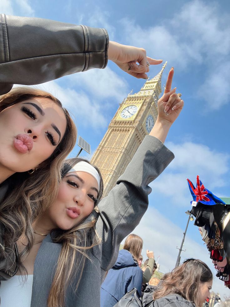 two young women standing next to each other in front of a clock tower