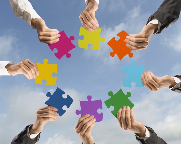 several people holding puzzle pieces together in the shape of a circle against a blue sky