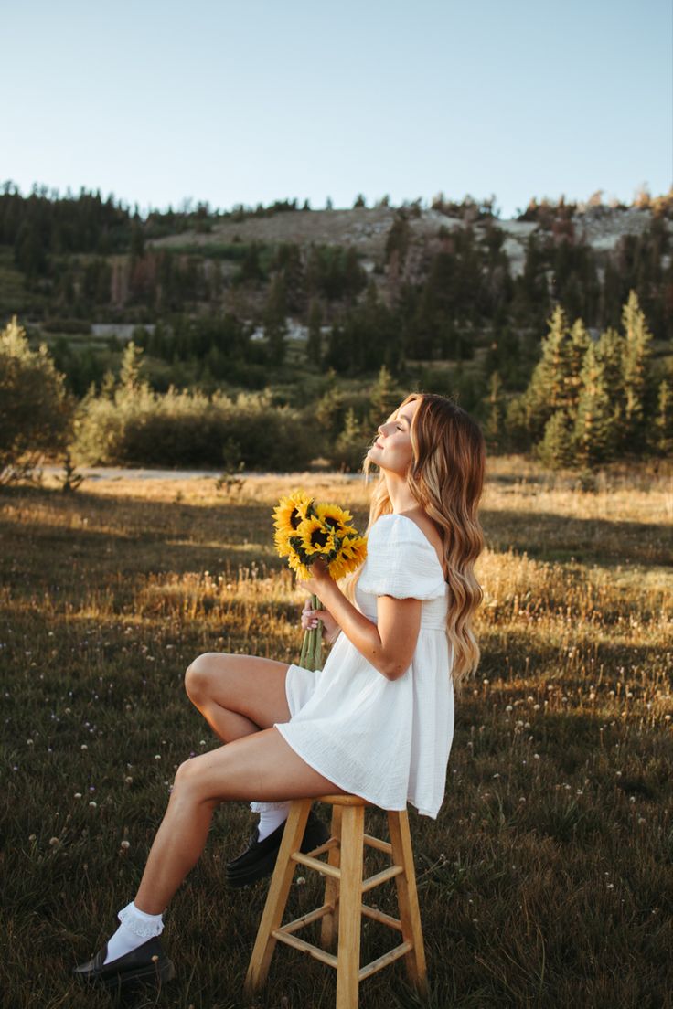 a woman sitting on top of a wooden stool holding a bouquet of sunflowers