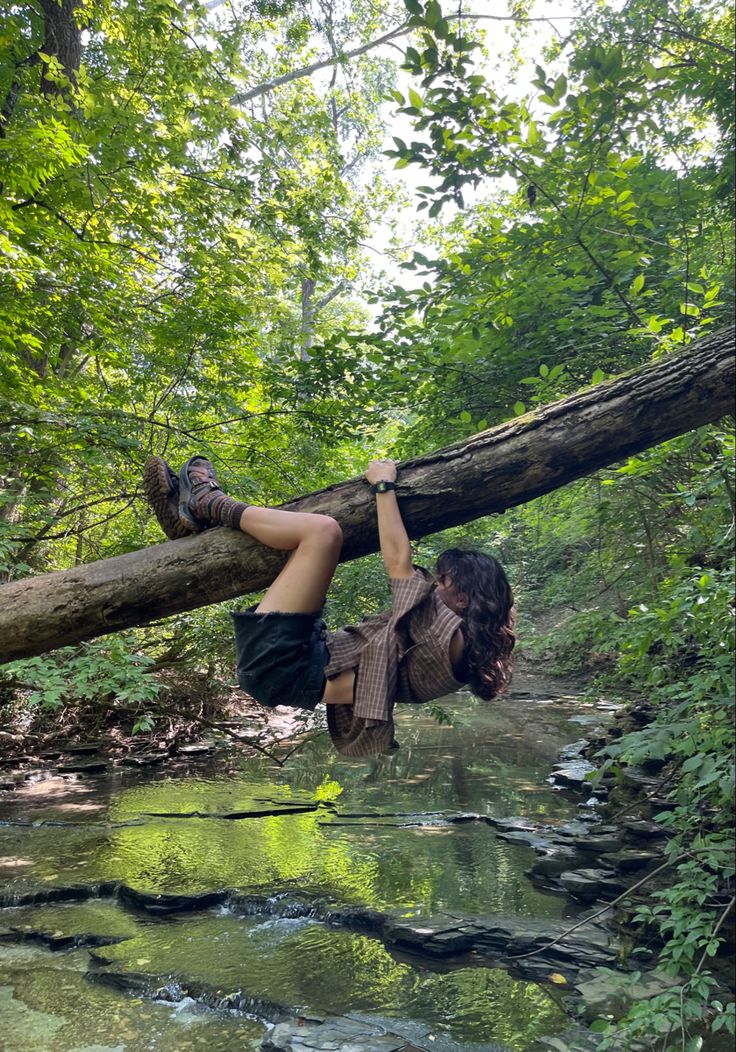 a woman hanging from a fallen tree over a river