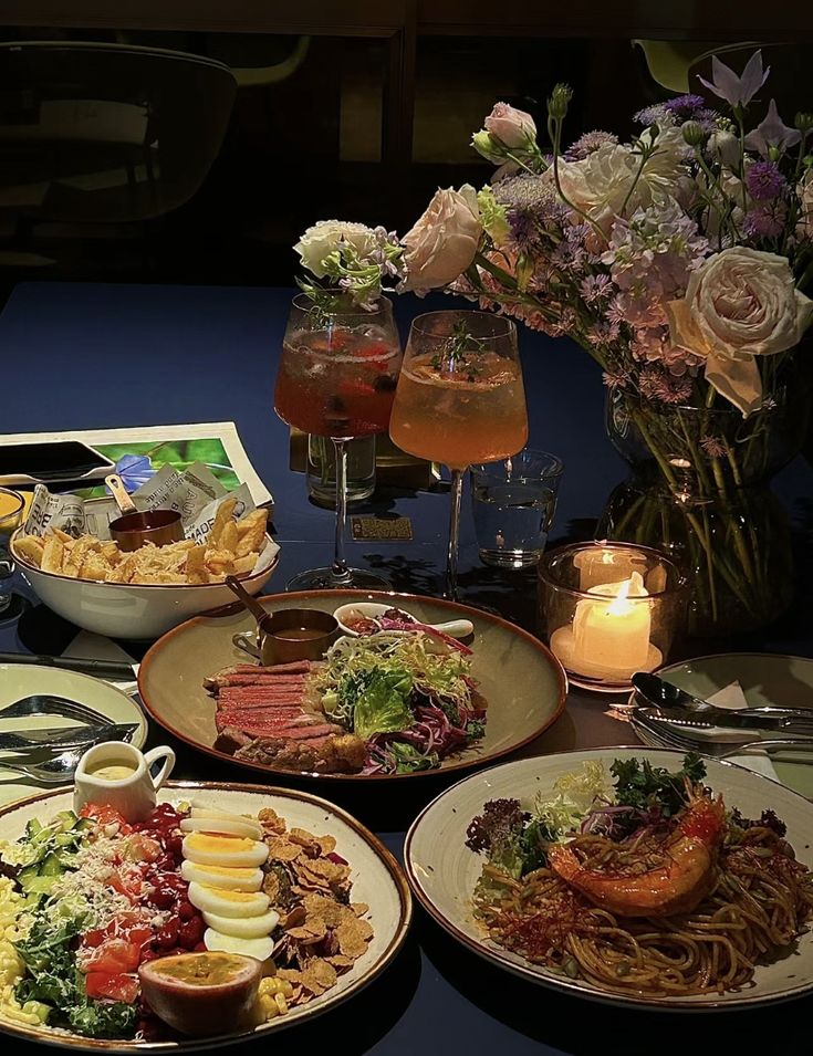 a table topped with plates of food next to glasses of wine and flowers in vases