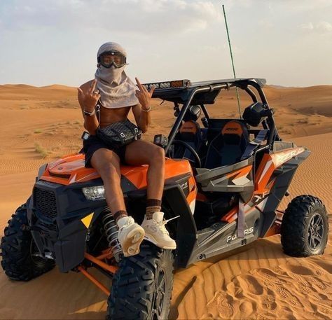 a man sitting on top of an orange and black dune buggy in the desert