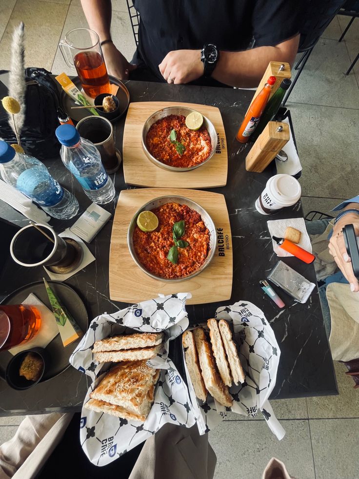 three bowls of food sit on a table with people sitting at it and eating sandwiches