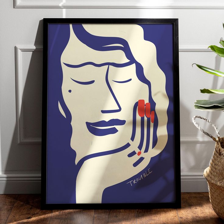 a framed poster with a woman's face on it next to a potted plant