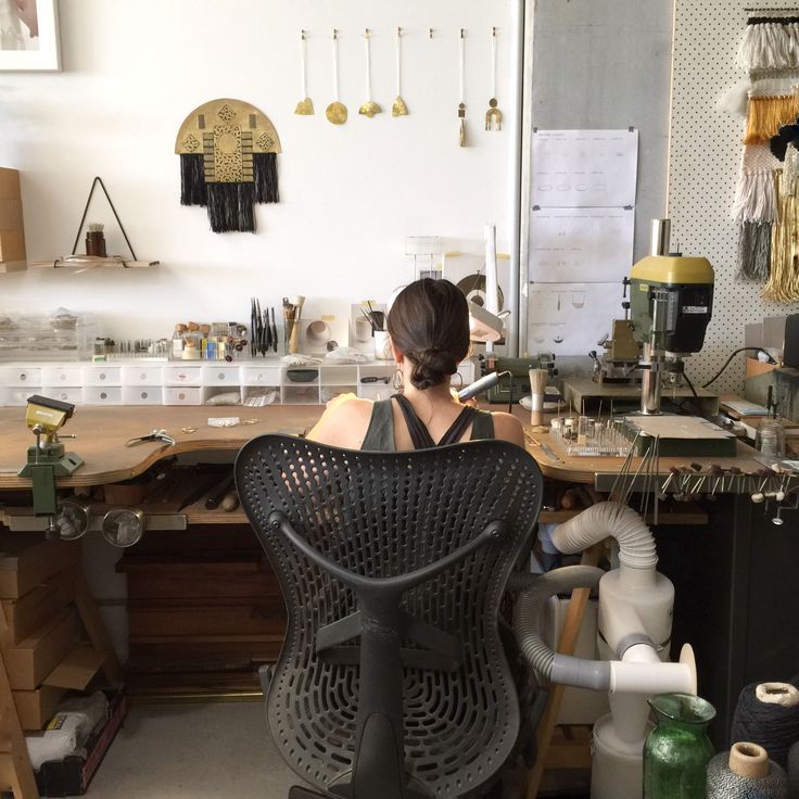 a woman sitting at a desk with lots of crafting supplies on top of it