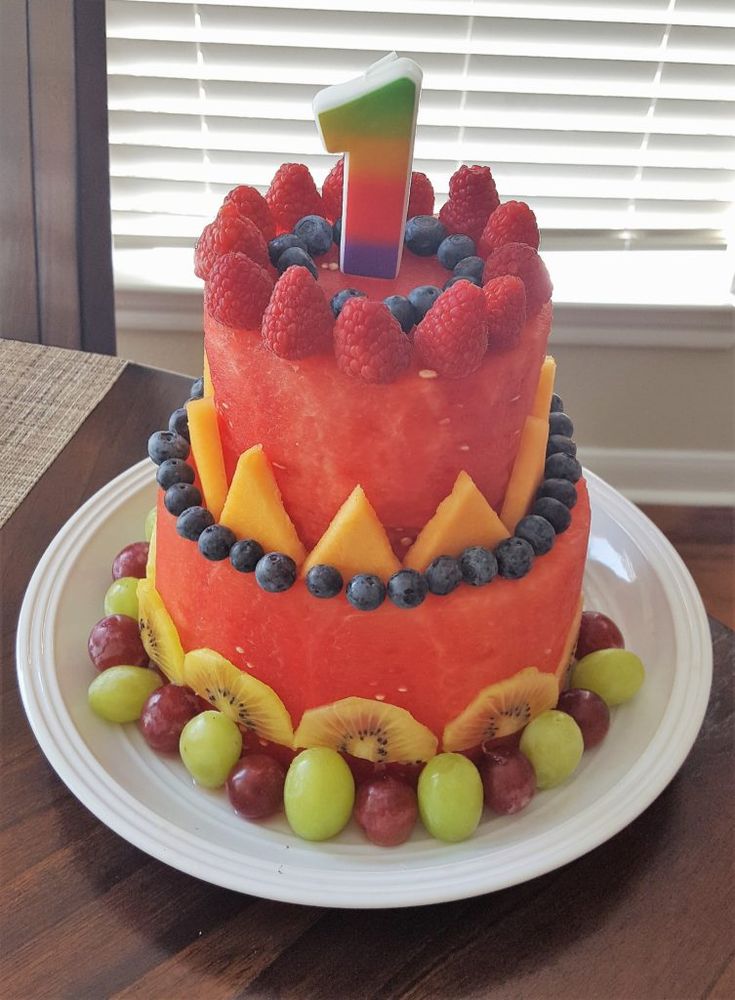 a watermelon and blueberry birthday cake with the number one on top, surrounded by fruit