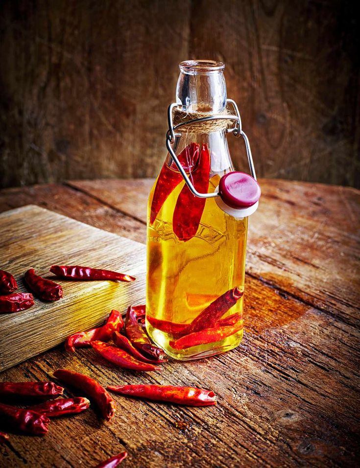 a glass bottle filled with hot sauce sitting on top of a wooden table next to red peppers