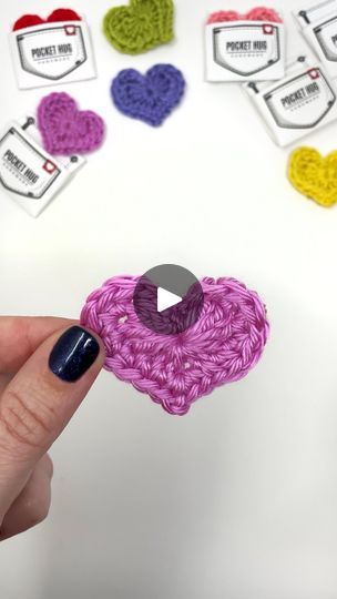 someone is holding up a crocheted heart brooch in front of several hearts