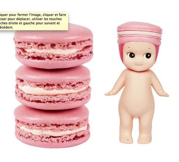 a toy doll standing next to a stack of pink macaroons