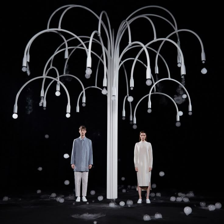 two men standing next to each other in front of a chandelier filled with white balls