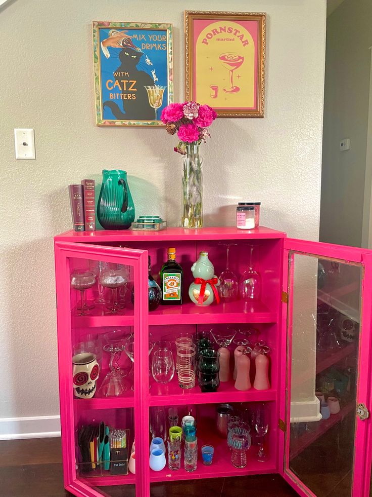 a pink cabinet with lots of bottles and glasses on it's shelves in a room