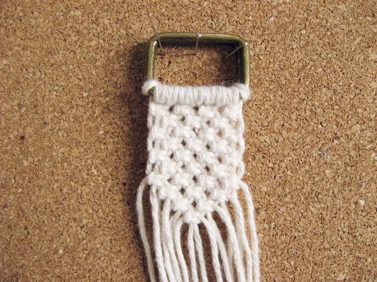 a piece of crocheted material is laying on the floor next to a metal hook