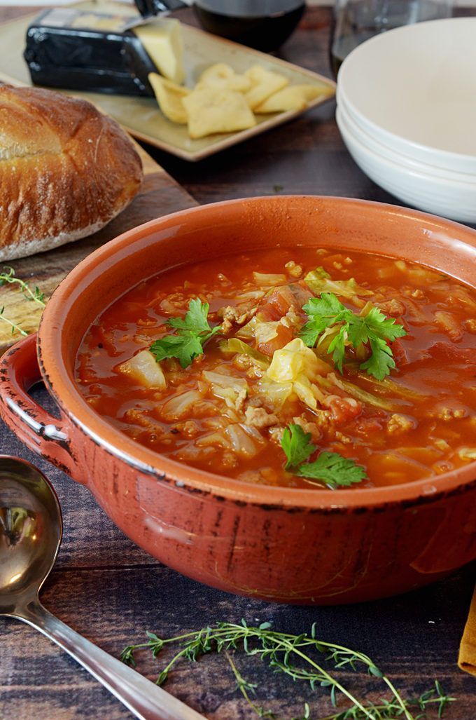 a bowl of soup on a table with bread and other food items around the bowl