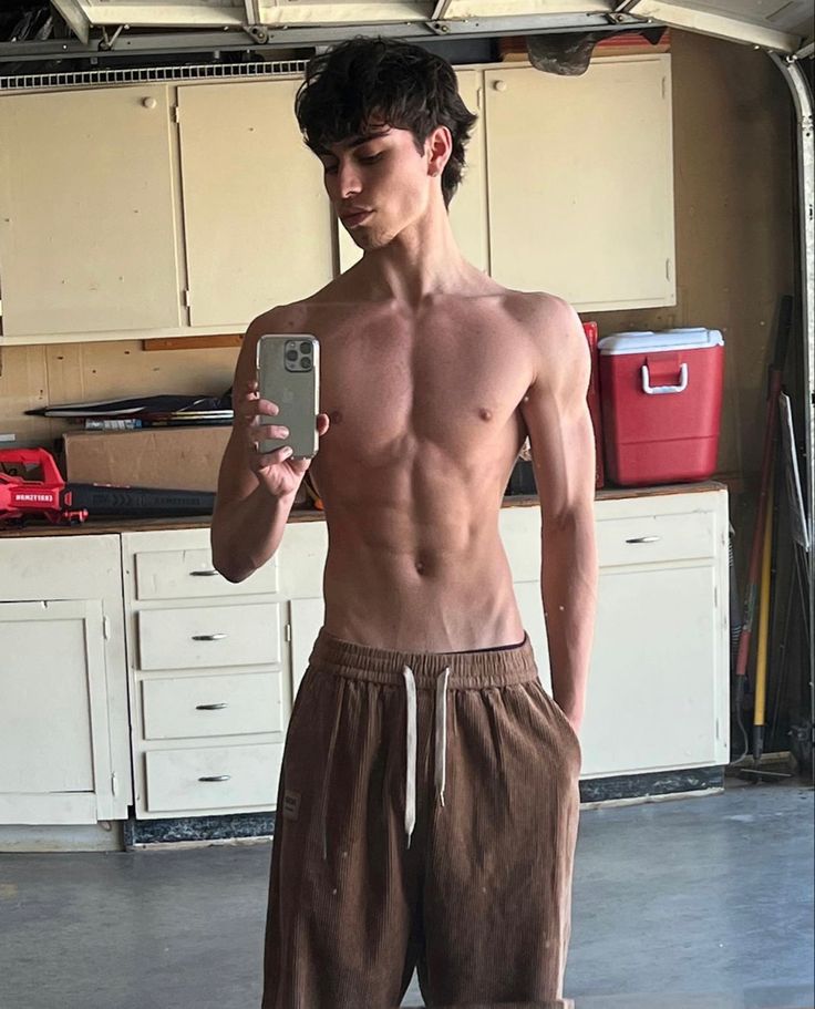 a shirtless young man taking a selfie in the garage with his cell phone