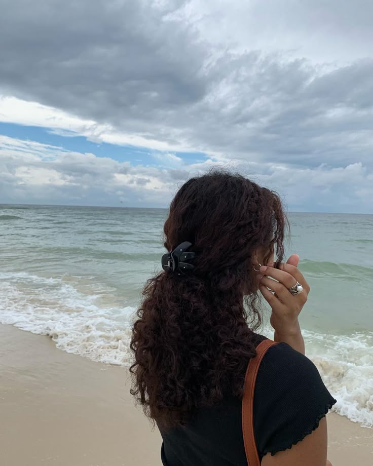 a woman standing on top of a beach next to the ocean holding a cell phone