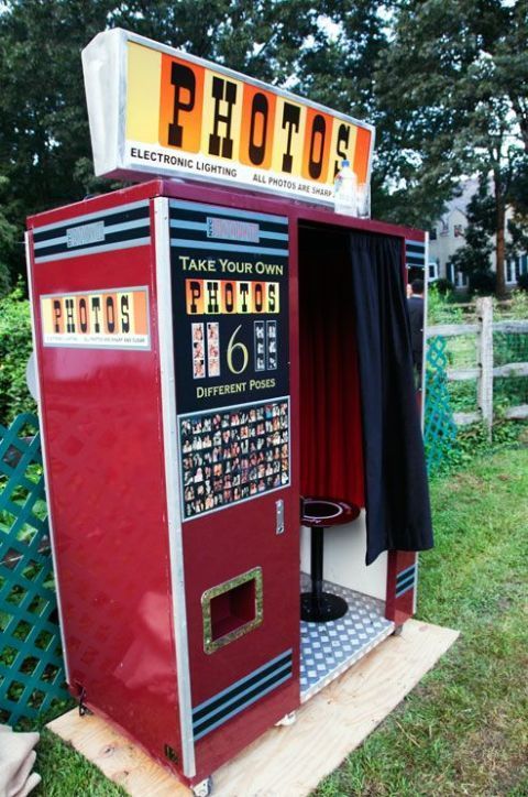 an old fashioned photo booth is in the grass near a fence and some trees with red curtains on it