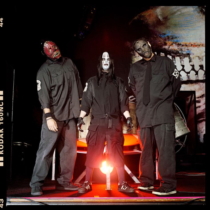 three men in black outfits standing on stage with one man wearing a mask and the other holding a flashlight