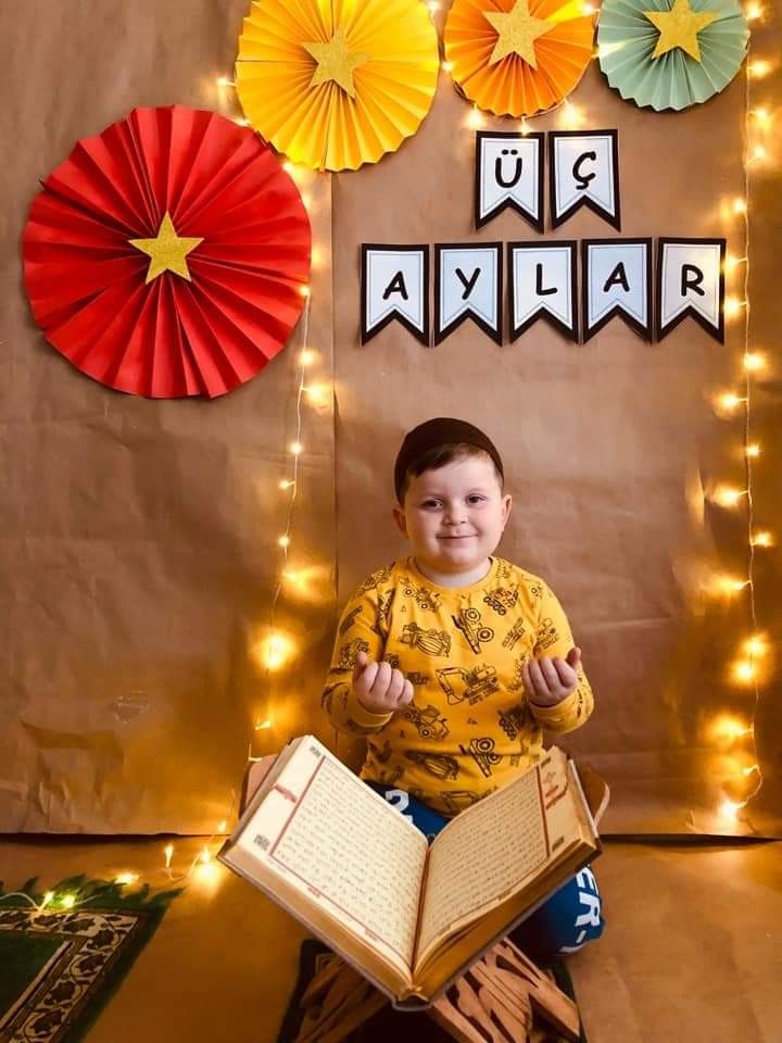 a young boy sitting on the floor with an open book in front of him and decorations behind him