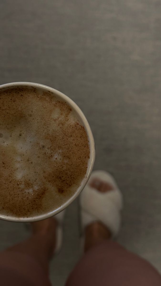 a person holding a cup of coffee with their feet on the ground in front of them