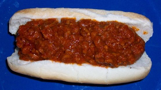 a hot dog with chili on it sitting on top of a blue tableclothed surface