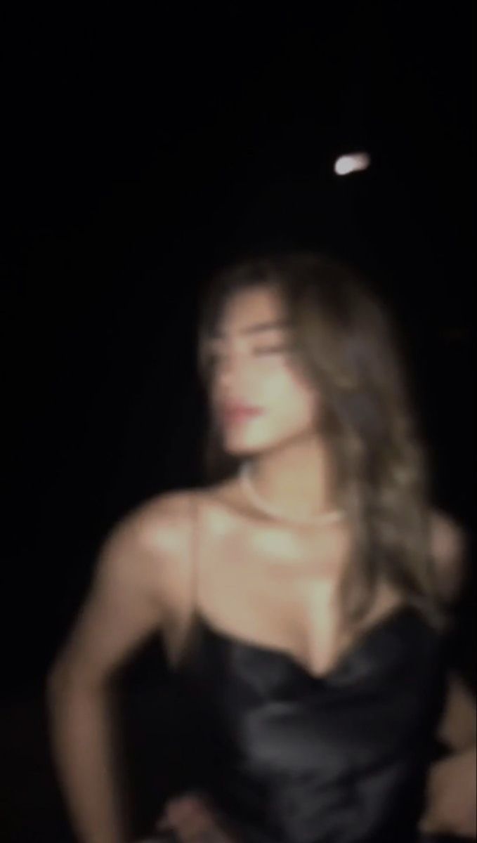 a blurry photo of a woman in a black dress at night with her hands on her hips